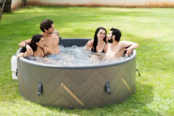 Four adults relaxing in an MSpa Mono 6 inflatable hot tub outdoors on a grassy lawn.
